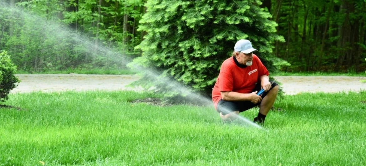 Photo of a Transitions Ourdoor Services teammember inspecting the water flow of a sprinkler head in a client's backyard.